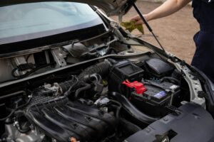 Mechanic inspecting car engine bay and battery during routine maintenance.